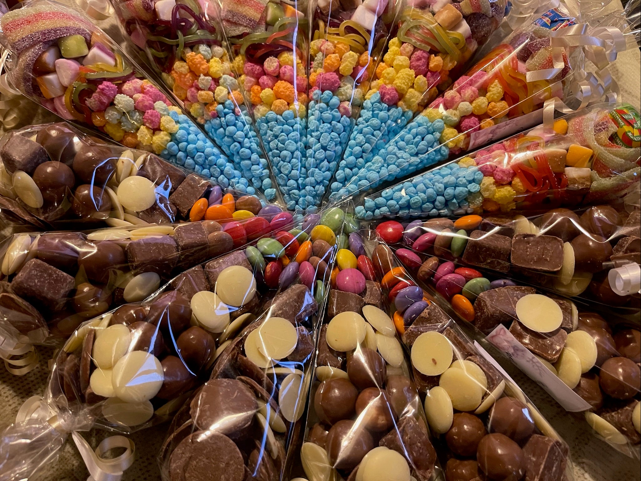 Sweet and chocolate cones that are laid spiraled on a table. They are filled with bright and colourful sweets.